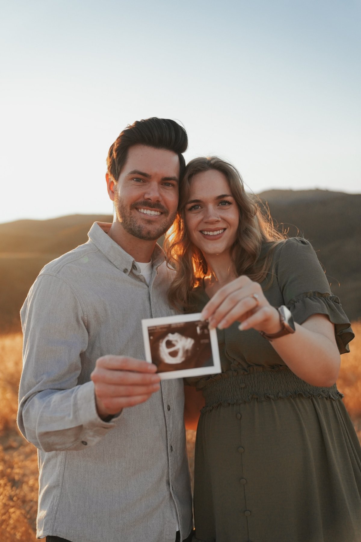 Couple holding an ultrasound photo at golden hour in the hills