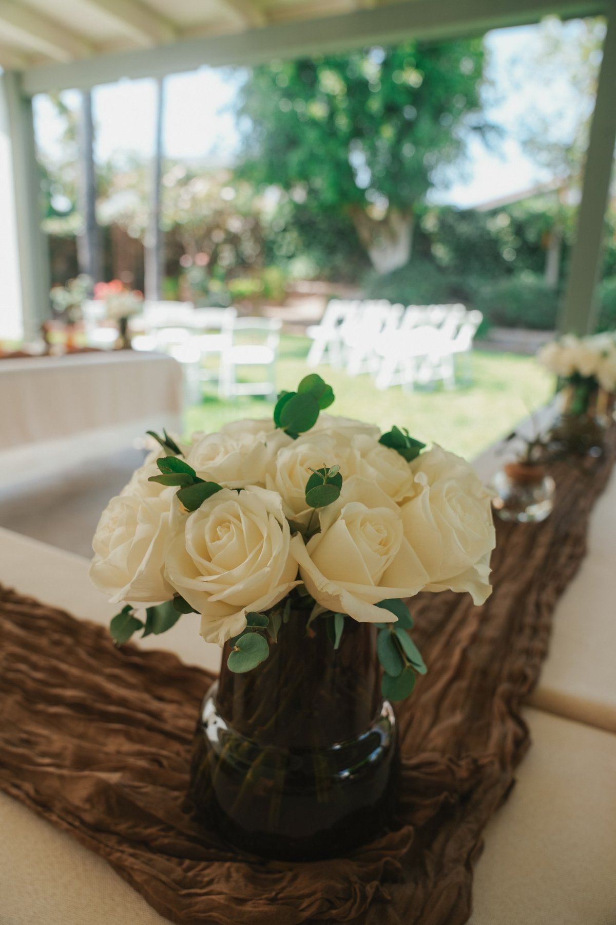 Cream roses with eucalyptus in a dark vase on a cheesecloth runner