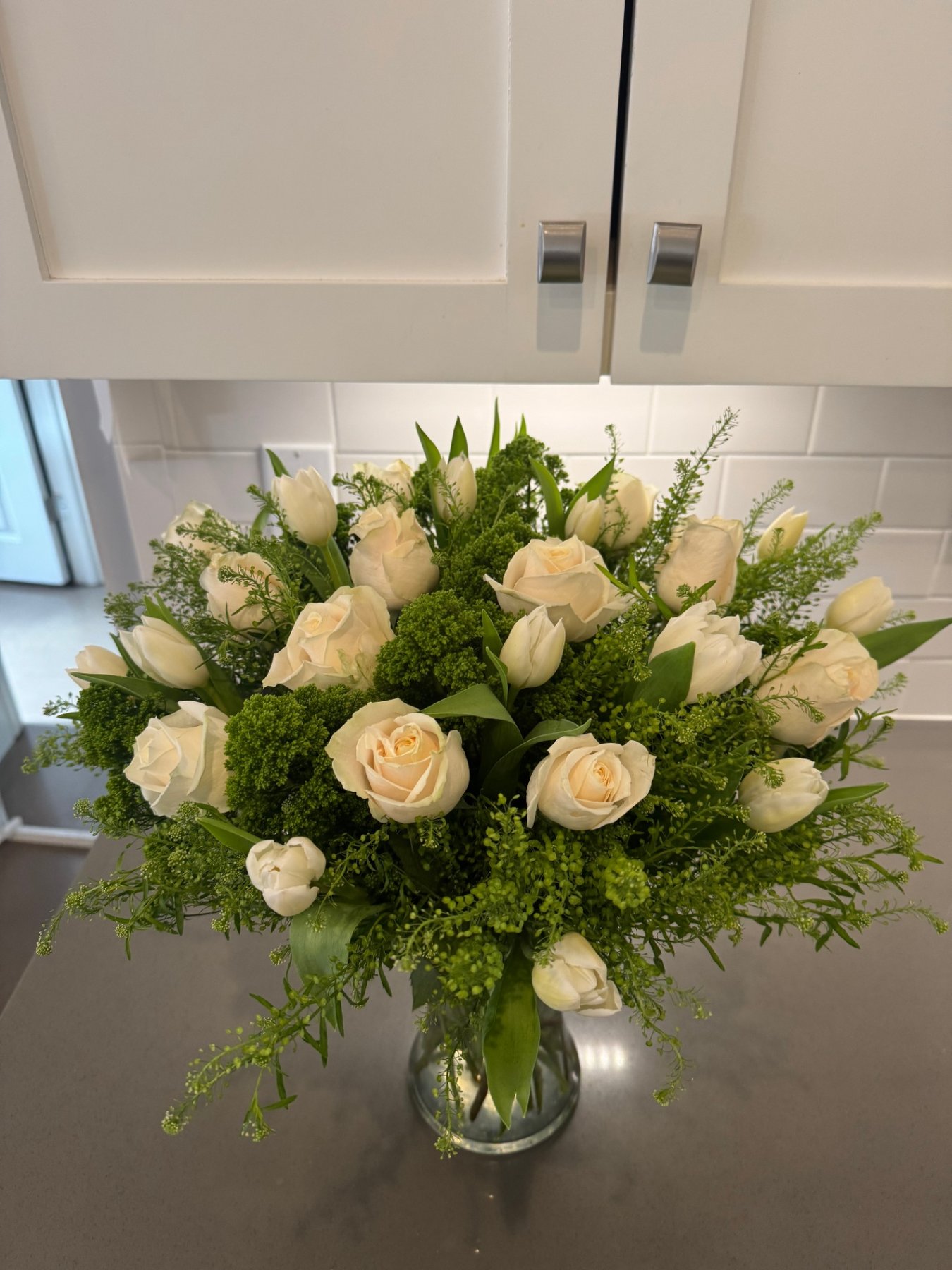 White roses and tulips with fresh greenery arranged in a glass vase