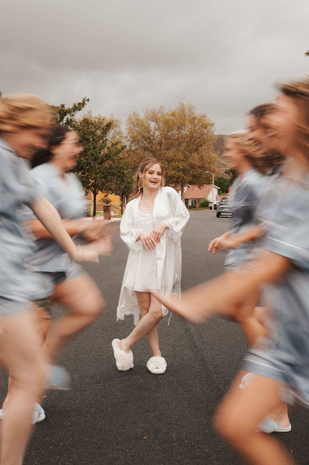 Bride in white robe surrounded by bridesmaids in motion