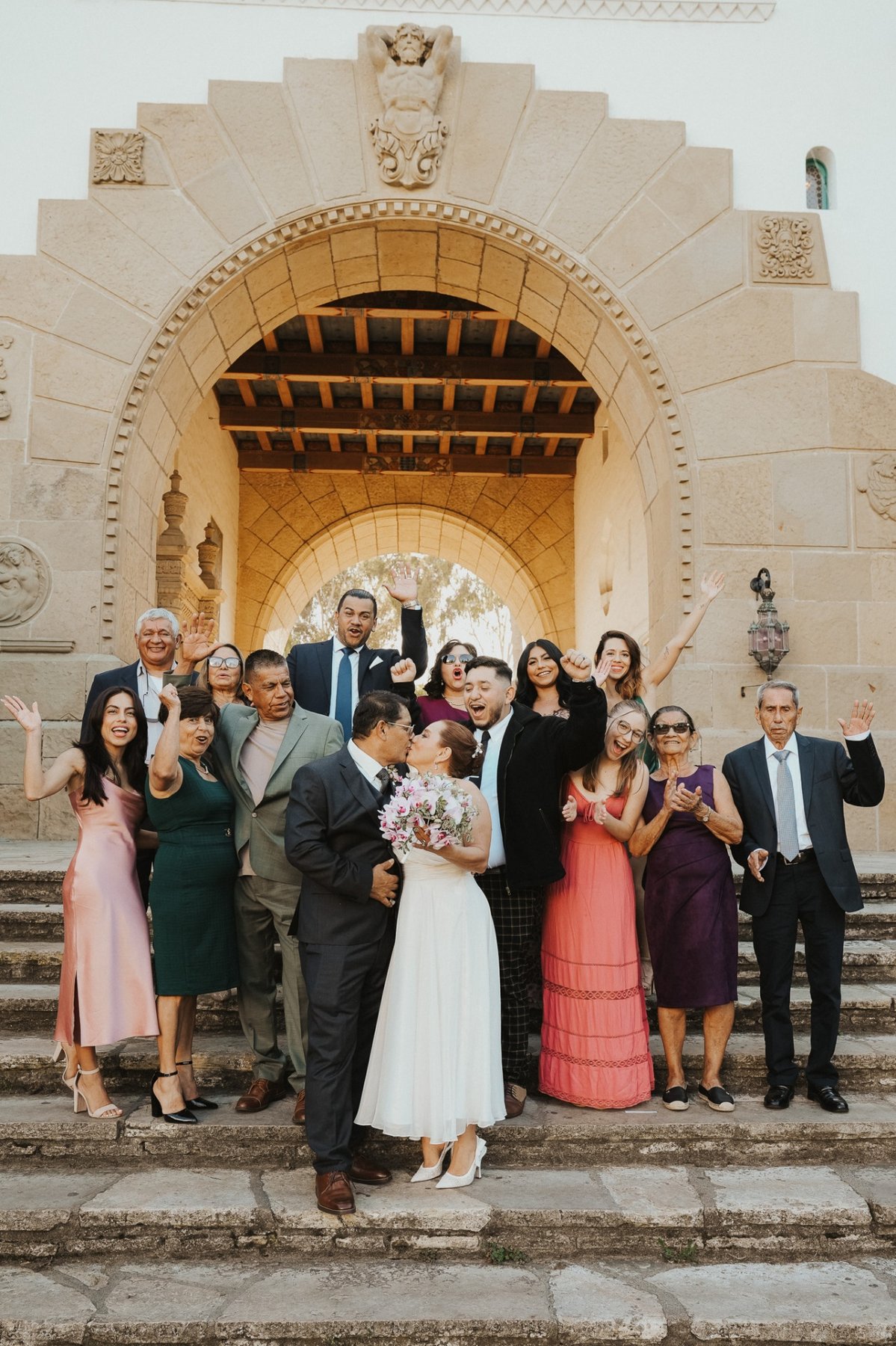Wedding family cheering around the couple kissing on historic stone steps
