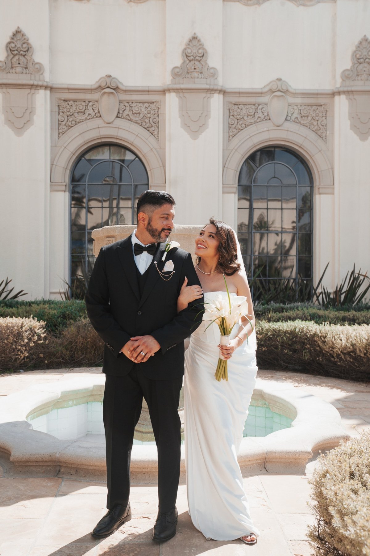 Bride and groom arm in arm before a Spanish-style courtyard fountain